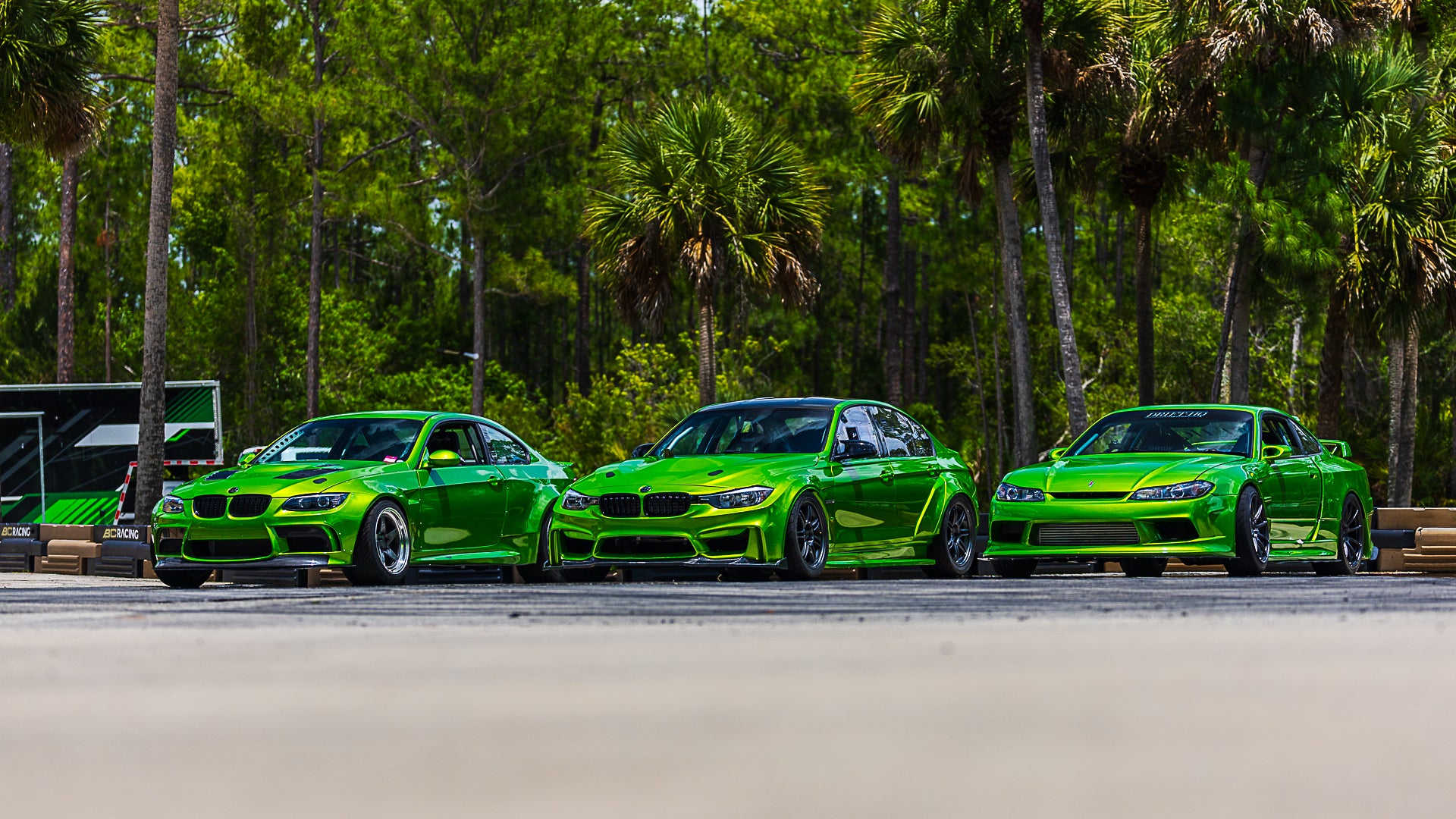 Three green sports cars parked on a road with palm trees in the background